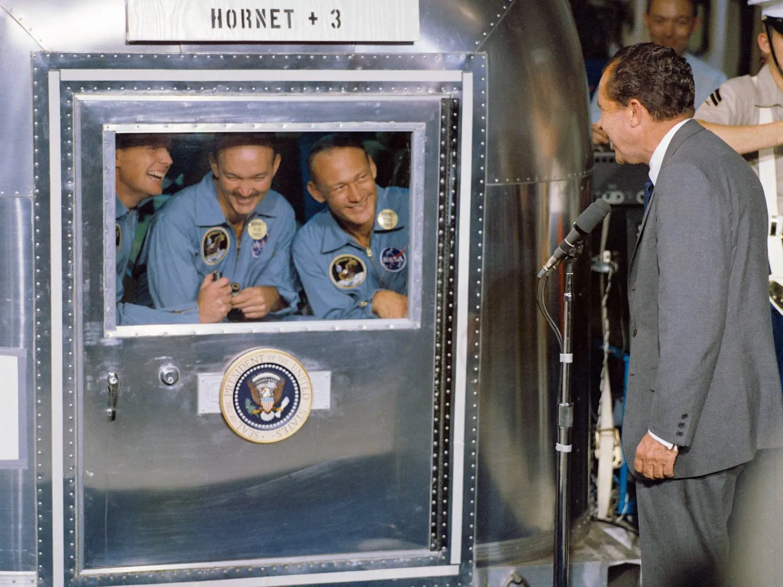 President Nixon welcomes Armstrong, Collins and Aldrin, sealed in the Mobile Quarantine Facility aboard USS Hornet, 24 July 1969