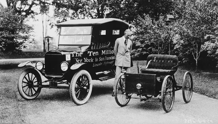 Henry Ford between the ten millionth Model T and his first car, the 1896 Quadricycle, 1924.