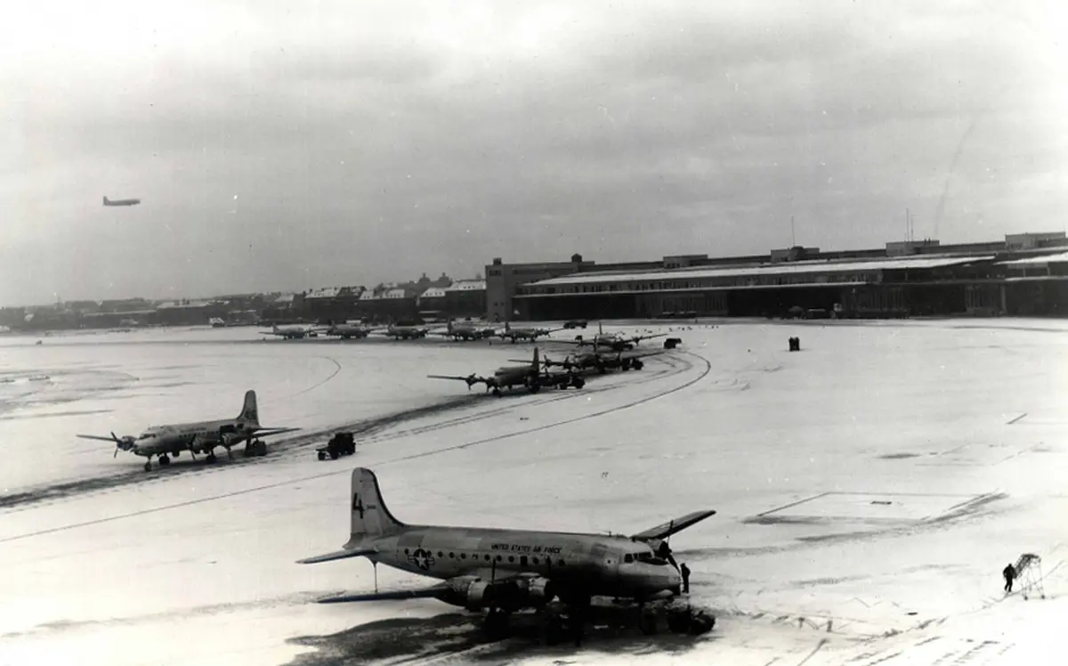 C-54s unload on Tempelhof’s snow-covered ramp while another transport comes in overhead. The airlift delivered supplies to Berlin every single day.
