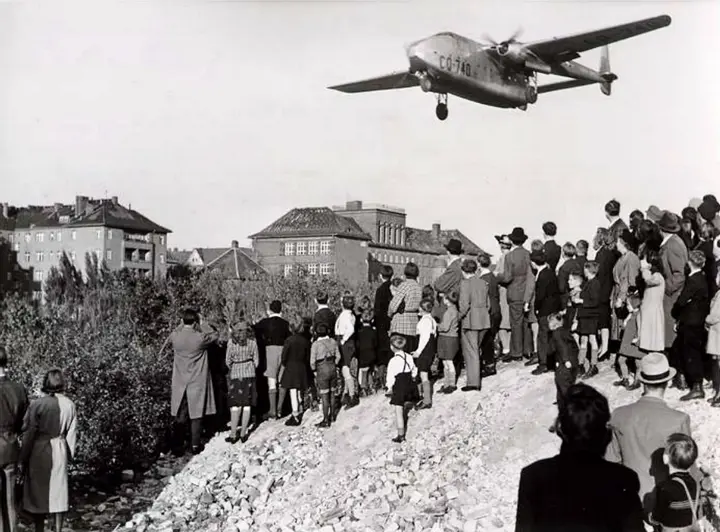 Berliners on a mound of rubble watch an American C-82 Packet come in low over the city, 1948.