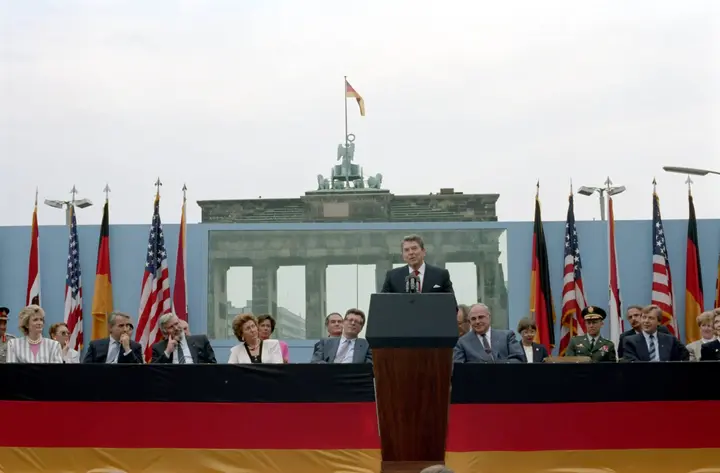 Reagan at the podium behind panes of bulletproof glass, the Brandenburg Gate at his back, 12 June 1987