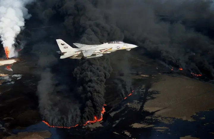 A Navy F-14A Tomcat of Fighter Squadron 114 flies over a Kuwaiti oil well set ablaze by Iraqi troops, 1991.