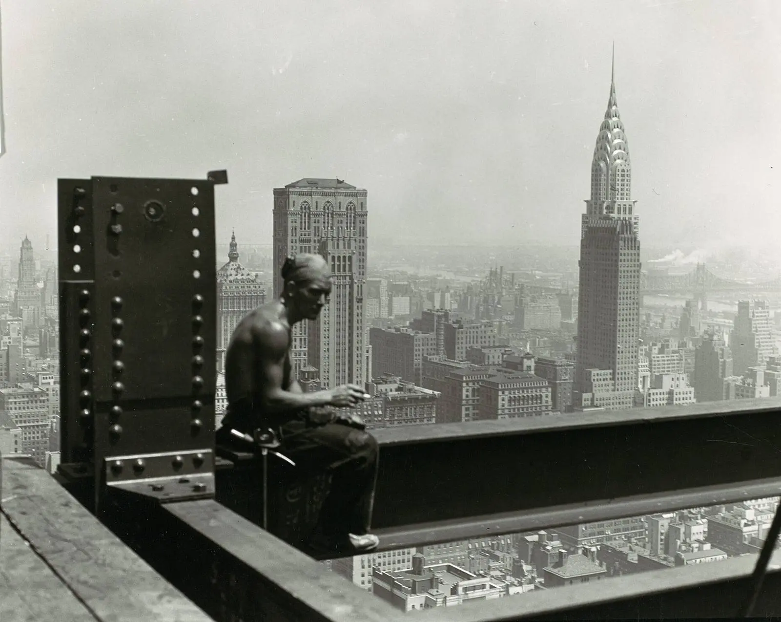 A worker takes a break on a beam hundreds of feet above Manhattan, with the Chrysler Building on the skyline.