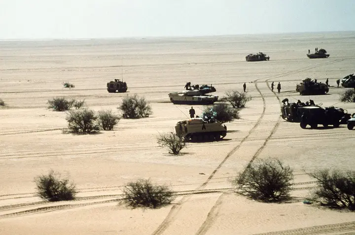 M1A1 Abrams tanks and armored vehicles of the 3rd Armored Division move out across open desert during Operation Desert Storm.