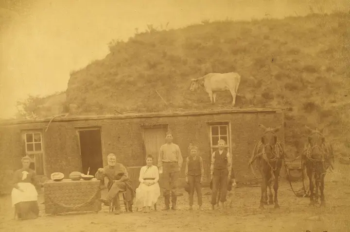 The Sylvester Rawding family in front of their sod house north of Sargent, Custer County, Nebraska, in 1886, with a cow on the sod roof.