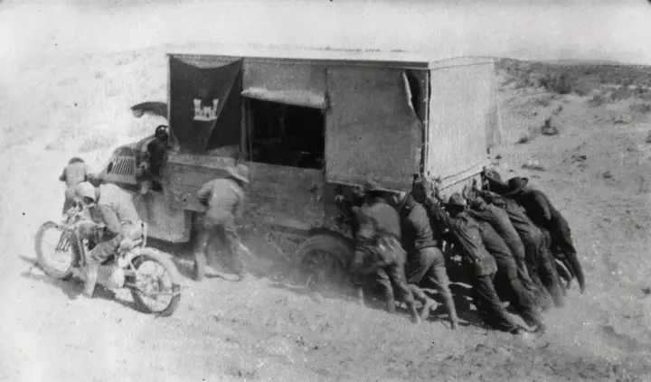 Soldiers of the 1919 Army transcontinental convoy put their shoulders to an engineer truck stuck in desert sand.