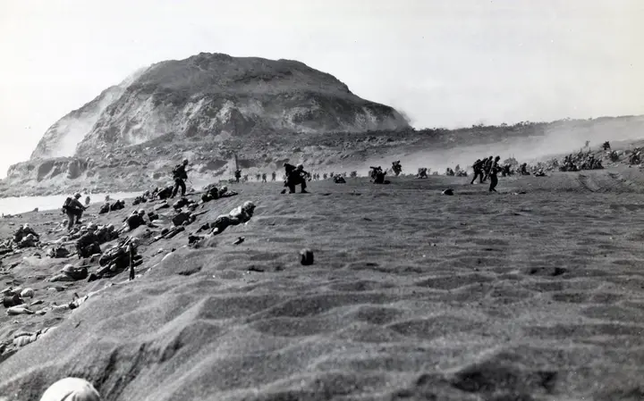 Marines charge inland across the volcanic sand at the foot of Mount Suribachi, 19 February 1945