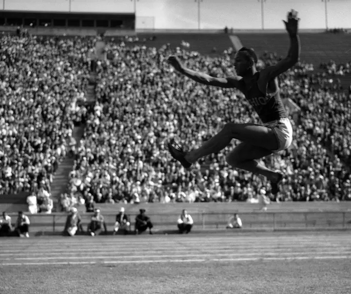 Owens in mid-flight over the long jump pit before a packed stadium in California in the 1930s