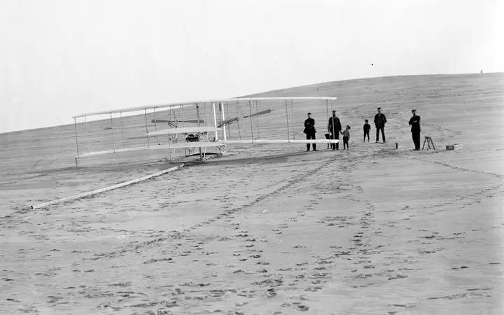The 1903 Flyer on its launching rail at Big Kill Devil Hill with men from the Kill Devil Hills Life-Saving Station, before the trial of December 14, 1903