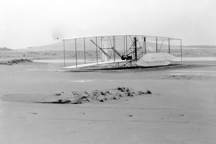 The 1903 Flyer on the sand after the fourth and longest flight, the frame of its front elevator broken on landing, December 17, 1903
