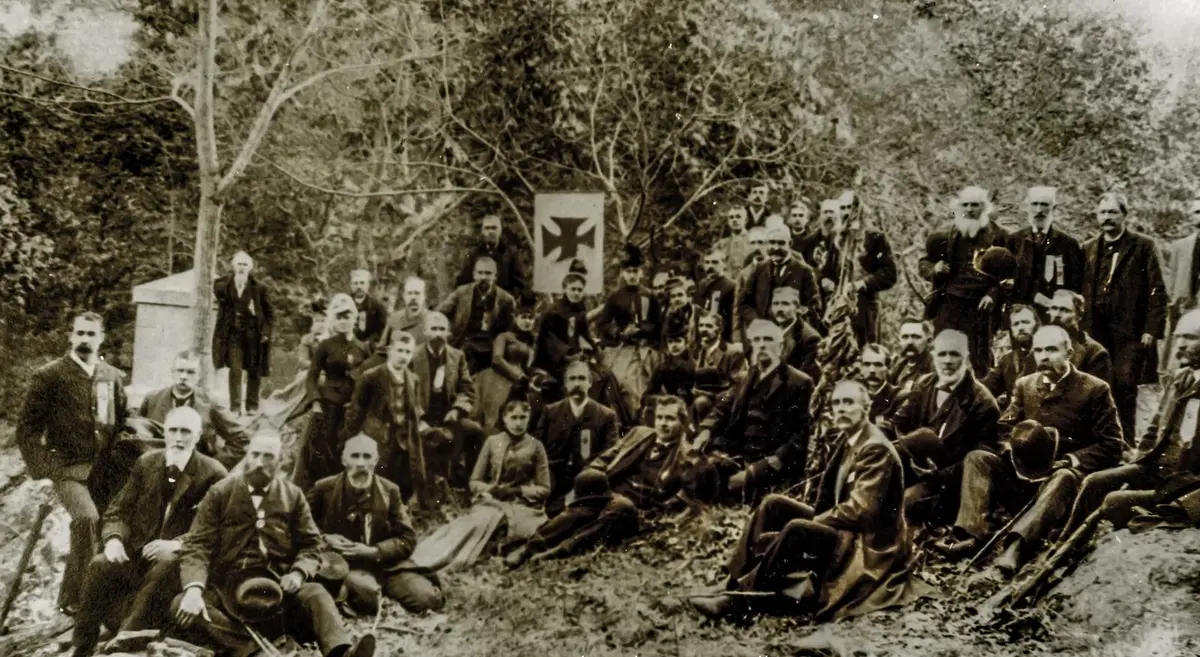 Veterans of the 20th Maine gather on Little Round Top in 1889, with Chamberlain seated at center right between the Fifth Corps cross and the regimental flag.