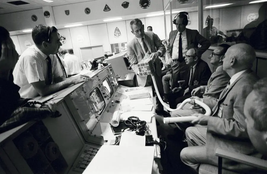 Deke Slayton (checked jacket) shows the ground-built prototype of the carbon dioxide adapter in Mission Control, 15 April 1970 (S70-35013)