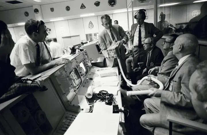 Deke Slayton (checked jacket) shows the ground-built prototype of the carbon dioxide adapter in Mission Control, 15 April 1970 (S70-35013)