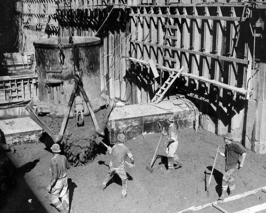 Concrete sluices from an eight-cubic-yard bucket into a column form as workers spread the pour, September 27, 1933
