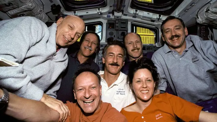 The STS-61 crew on Endeavour’s flight deck with Hubble berthed in the payload bay, December 1993 (STS061-05-031).