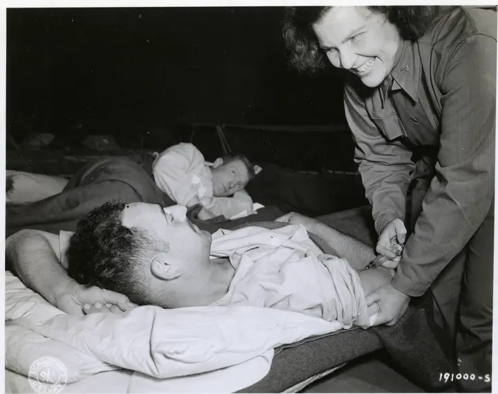 Army nurse Lt. Gertrude A. Nolan gives an injection to Sgt. Charles A. Comar of New York City in an evacuation hospital in Normandy, 5 July 1944.