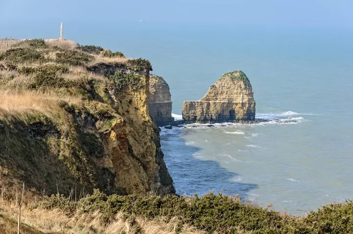 The tip of Pointe du Hoc today, with the granite dagger of the Ranger Monument standing on the cliff top above the sea stack.