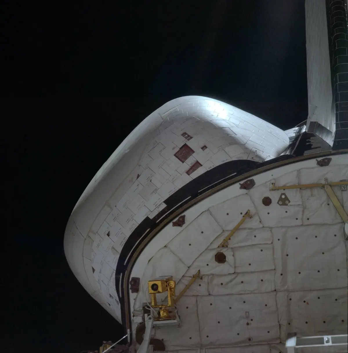 From the cabin, the crew photographs dark squares on Columbia’s left engine pod where heat-shield tiles shook loose during launch (STS001-08-289)